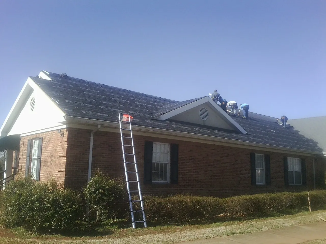 Crew tearing shingles off a brick ranch roof with a ladder set — Emergency Roof Repair work by our crew in Livonia