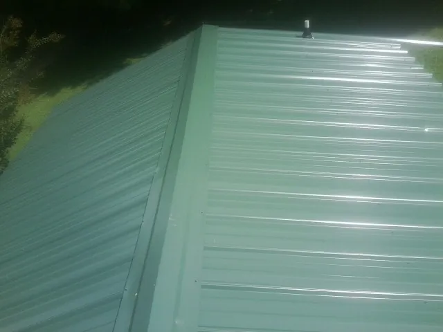 New green metal panels meeting at the ridge of a roof — Flat Roof Repair work by our crew in Livonia