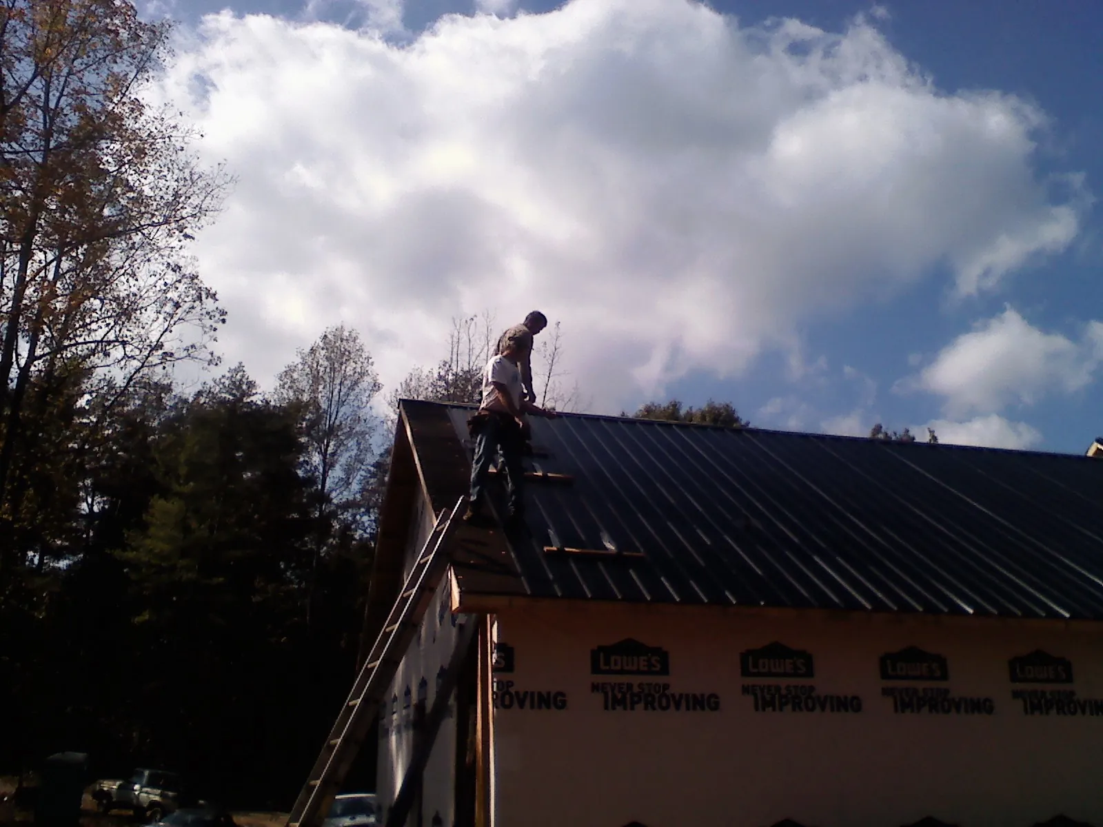 Roofer fastening dark metal panels high against a cloudy sky, from a Roof Inspection job in Livonia