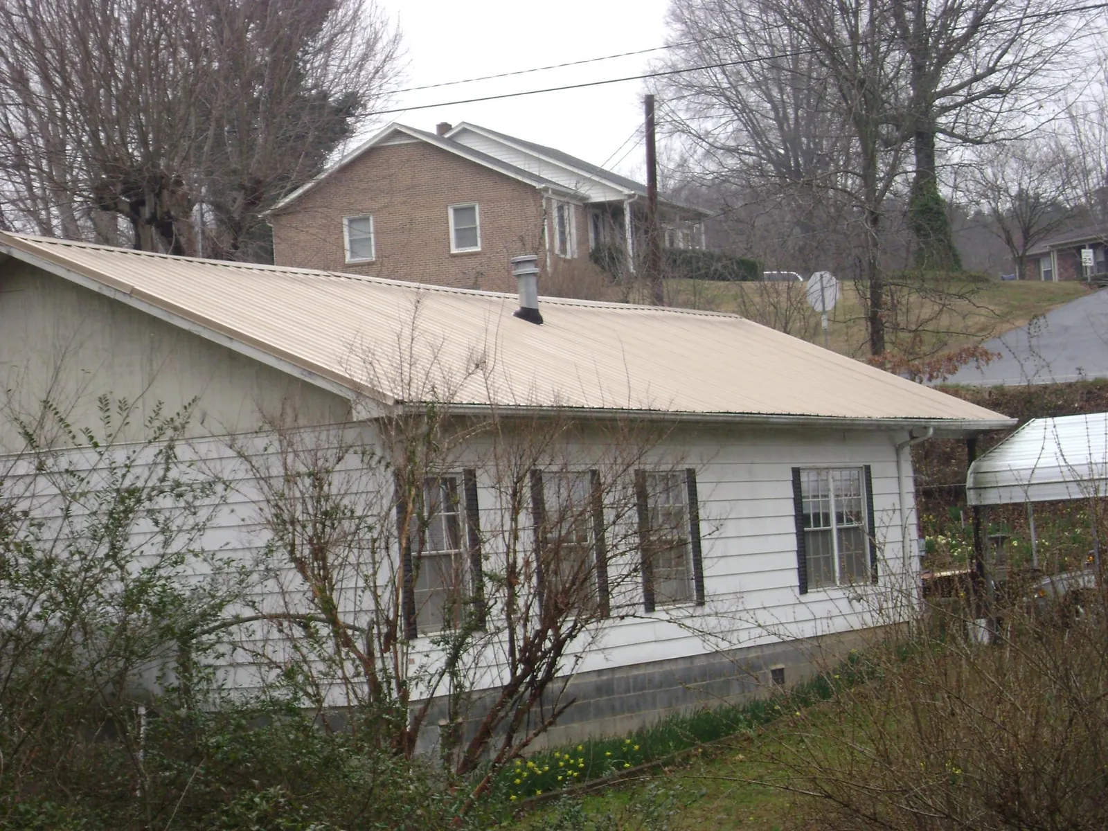 Tan metal roof on a white sided house set into a hillside — Commercial Roofing by Roofing Brothers in Livonia