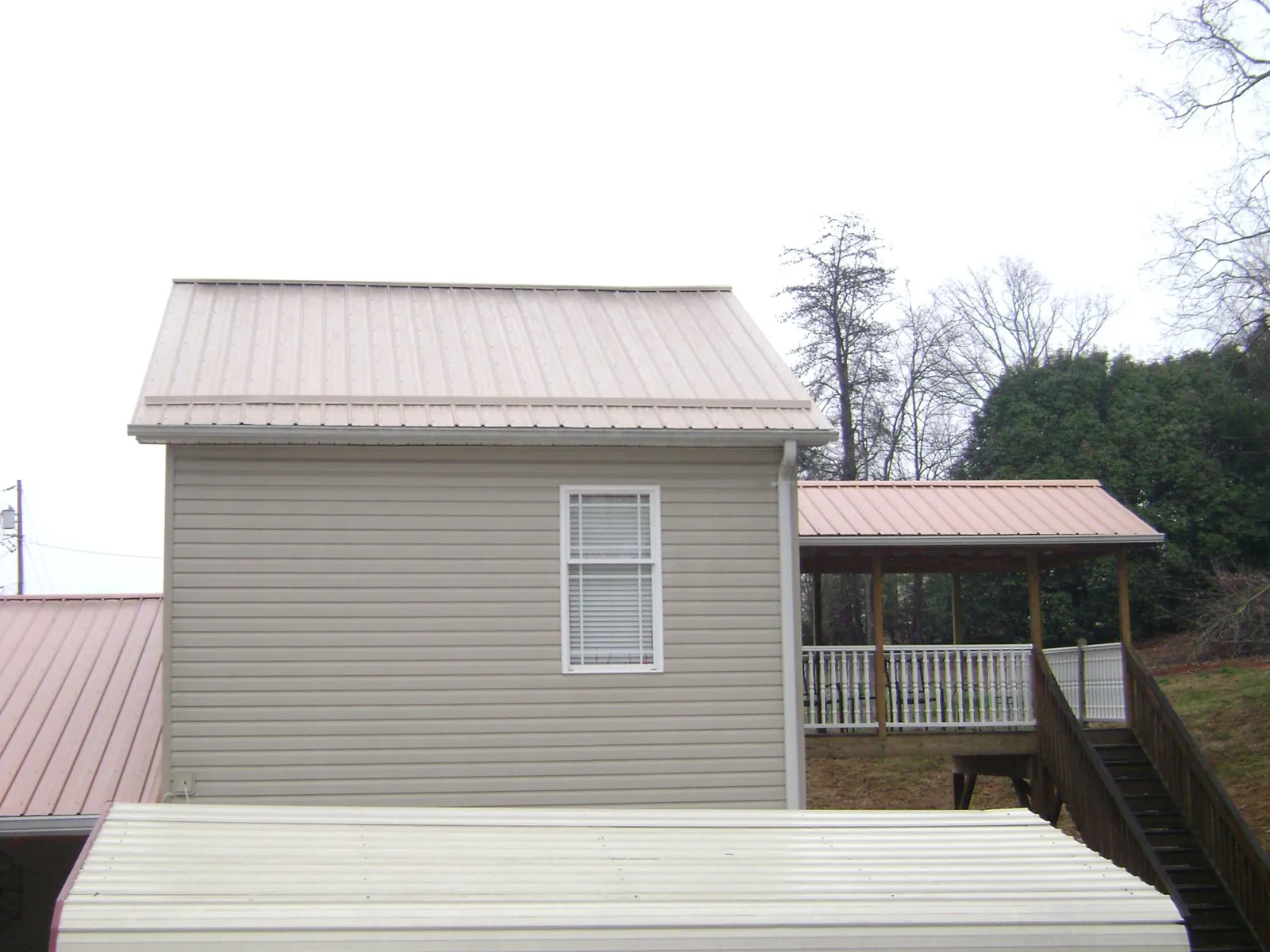 Tan metal roofs on a two story addition and attached porch, from a Roof Replacement job in Livonia